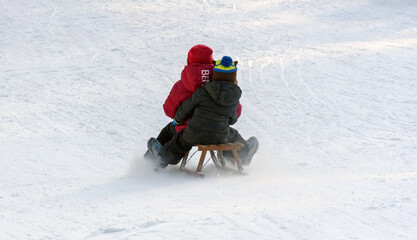 Back shot of kids riding a wooden sled down sledding hill on a sunny winter day