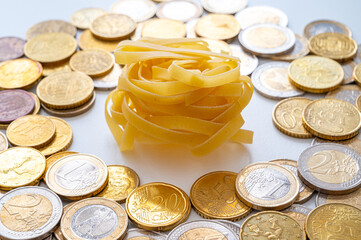 Noodles with coins around, on white surface. Rising price of pasta and shortage of wheat. 

