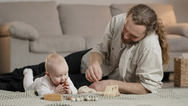 Happy adult parent dad helping cute infant newborn toddler son daughter playing toys together on floor caring father little kid boy girl having fun play constructor at home. Child development concept