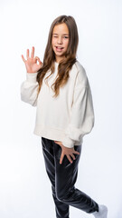 portrait of a girl in the studio. beautiful little girl in a white sweater and trousers smiles, points ok and winks. isolated white background