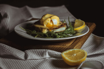 Eggs benedict and poached hollandaise sauce with arugula and lemon. Delicious food for breakfast. High quality photo