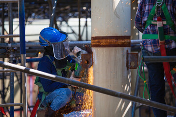 Worker using electric wheel spark grinding on welder metal carbon steel part pipe inside tank