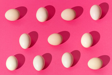 Creative pattern done with white eggs on trendy pink background. Minimal easter, spring mockup. Contemporary style. Natural sun light lighting and sharp shadows.