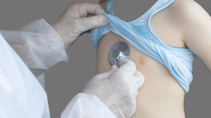 doctor or nurse, pediatrician, is examining a little boy with stethoscope. medical concept. health care and healthy lungs. respiratory infections prevention. grey back. space for text on neck,chest