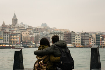 Fototapeta na wymiar two lovers girl and boy sitting against galata tower in bosphorus istanbul near the sea