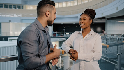 Friendly multiethnic business partners colleagues african woman and indian arabian man talking standing in modern company office hall two diverse employees having corporate discussion at work break