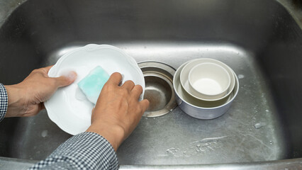 洗剤をつけたスポンジで食器を洗う