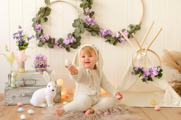 Cute funny baby with bunny ears and colorful Easter eggs at home