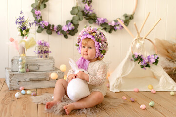 Sweet little girl with decoration on her head and colored Easter eggs on a white wooden background