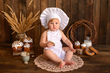 A little funny girl in a white cook suit on a dark wooden background