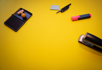 Top view of a wooden stamp with ink, stapler, sticky notes and markers isolated on yellow background