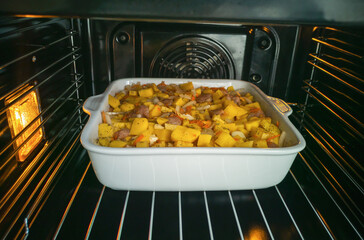 Cooking homemade food in an electric oven. Vegetable stew with potatoes, meat and herbs in a white ceramic baking dish.