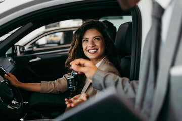 Happy and beautiful middle age business woman buying new car at showroom. A nice seller helps her make the right decision. He gives her the car keys.