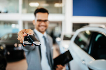Good looking, cheerful and friendly salesman poses in a car salon or showroom. He is looking at...