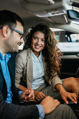 Happy middle age couple enjoying while choosing and buying new car at showroom. They are sitting inside of car.