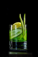 Cocktail with cucumber, ice on bar counter in a restaurant, pub. Fresh tonic drink with lime juice, mint, gin, cucumber juice. Alcoholic cooler beverage on black isolated background