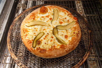 Freshly baked pizza with cucumbers and mozzarella comes out of modern conveyor oven