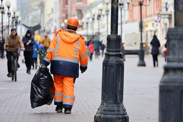 Worker carries a garbage bag down the street on people background. Cleaning the city streets