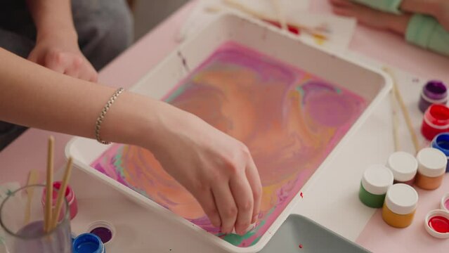 Young woman puts egg into tray with mix for marbling design