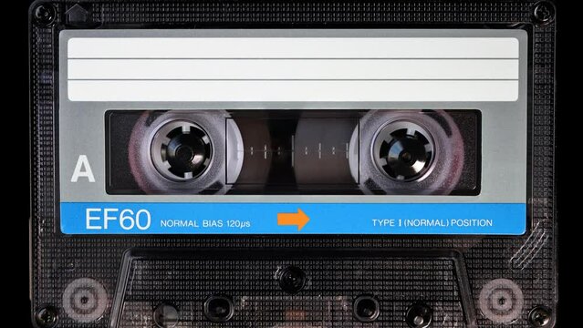 Audio cassette tape in use for sound recording in the tape recorder. A vintage, brand new blank blue labelled music cassette playing back in a deck player. Static video camera shot. Close up, 4K
