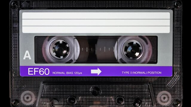 Audio cassette tape in use for sound recording in the tape recorder. A vintage, brand new blank purple labelled music cassette playing back in a deck player. Static video camera shot. Close up, 4K
