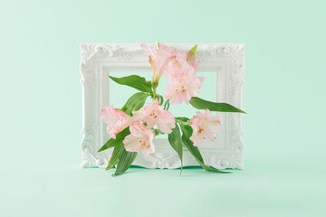 Creative spring arrangement made of white retro picture frame and pink lisianthus flowers on a green background. Minimal concept. Mother's day, wedding and springtime inspiration. Still life