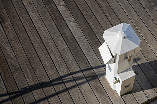 Clean, uncluttered, gray wooden dock with sculptural white electric power pedestal for boats, minimalist industrial art.