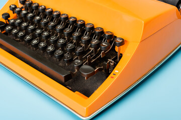 close up view of black keyboard of orange typewriter on blue.
