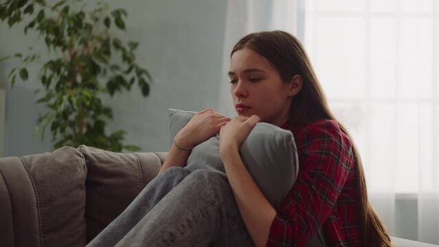 Pensive lady cries hugging pillow on sofa in living room
