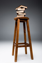 stack of books on wooden stool on grey background.
