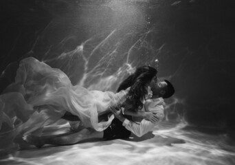 A romantic couple kissing underwater in swimming pool wearing clothes