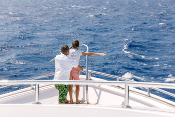 Family sailing on a luxury yacht. Back view of father and son on the ship. Father and son expending...