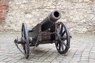 Old iron cannon on wheels near a high castle stone wall on a sunny day