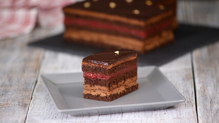 Sponge cake slice with chocolate mousse, jellied cherry jam topped with chocolate icing.