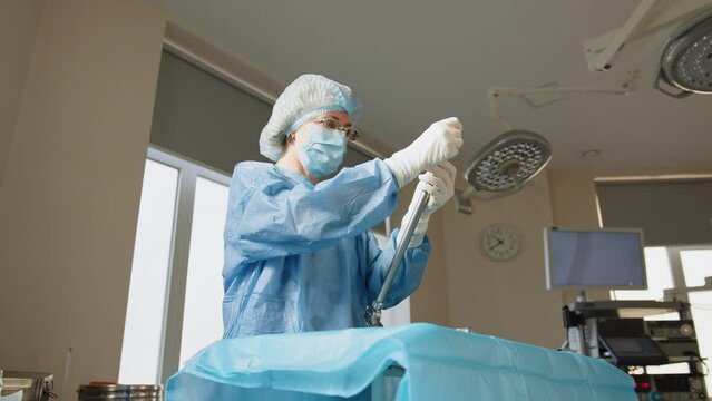 Portrait of a female healthcare worker in a protective mask standing at a table with surgical instruments. Surgical instrument. Surgeon holding an instrument for surgery. Preparation for laparoscopy.