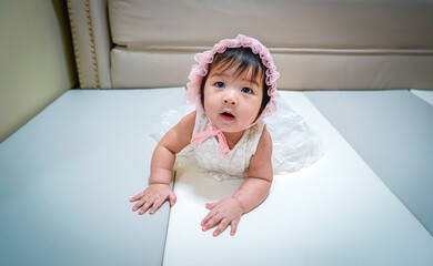 Little Baby Princess girl wear white dress with whit hood lying down on pad floor. Looking at camera