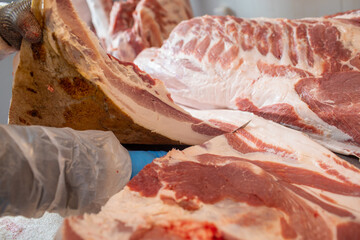 close-up of meat processing in the food industry, the worker cuts raw pig, storage in refrigerator,...