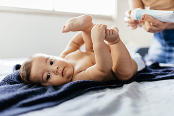 Mother changing baby's diaper in bed. Mother applies diaper rash cream. - obrazy, fototapety, plakaty