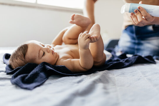 Mother Changing Baby's Diaper In Bed. Mother Applies Diaper Rash Cream.