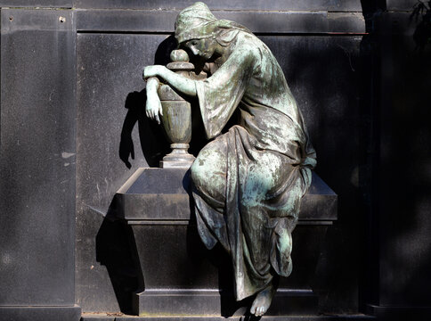 An old metal sculpture of a grieving woman who embrace an urn.