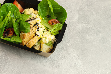 Salad take away. Healthy salad with different lettuce, corn, cauliflowers and chicken in black recyclable paper box on gray background. Copy space. Healthy restaurant food delivery concept.