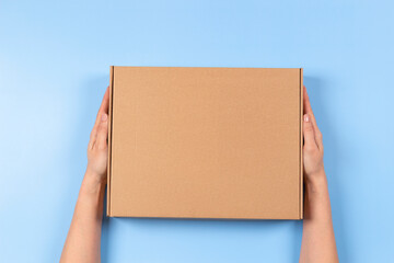 Top view to female hands holding brown cardboard box on light blue background. Mockup parcel box....