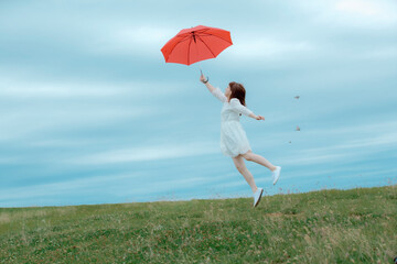草原で傘を持ってジャンプする女性