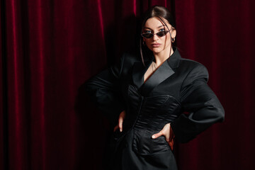 A model wearing all black posing in front of a red cinema curtain with nice sunglasses