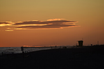 Lifeguard tower built on the shore of a sea and orange sky with few clouds on the top