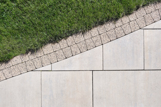 Combination of сoncrete slabs and paving tiles on the border with a lawn, top view.