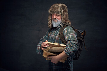 Strong old man with bag and stack of lumber against dark background