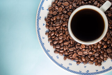 Many coffee beans and a traditional coffee cup on blue background