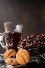 Some black coffee beans in a glass pot next to a cup of black coffee