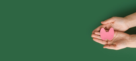 World Thyroid Day. Women's hands hold a paper form of the thyroid gland on green background....